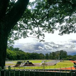 Empty bench on grassy field against cloudy sky