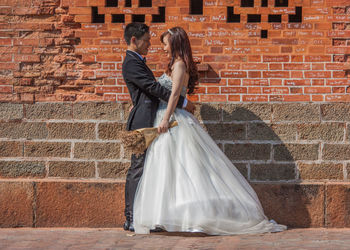 Rear view of woman with umbrella against brick wall