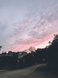 Road by silhouette city against sky at sunset