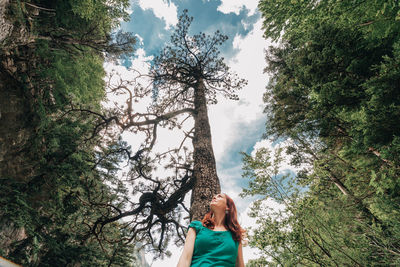 Low angle view of woman standing by trees against sky