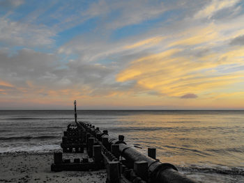 Scenic view of sea against sky during sunset with groyne and pipeline