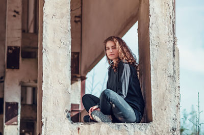 Curly cute young woman sitting in window of unfinished house. architecture, construction.
