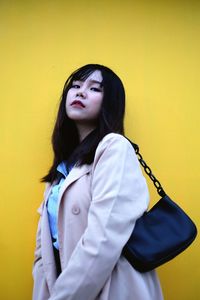 Young woman looking away while standing against yellow wall