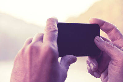 Close-up of man photographing through mobile phone against sky