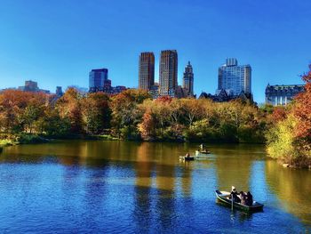 Trees and buildings by lake against blue sky