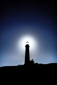 Low angle view of silhouette lighthouse against sky at night