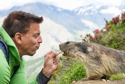 Profile view of man feeding marmot against mountains