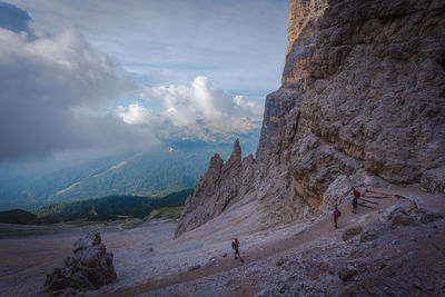 People on rocks by mountains against sky