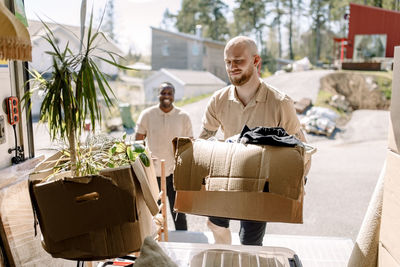 Multiracial movers carrying boxes from truck during sunny day