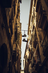 Low angle view of shoes hanging on wire amidst buildings against sky