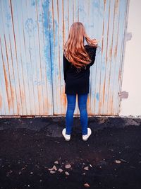Rear view of girl standing against corrugated iron