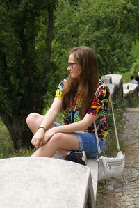 Young woman sitting on retaining wall at park