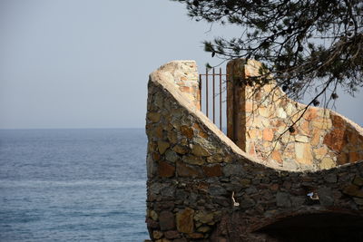 Stone wall by sea against clear sky