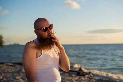 Man wearing sunglasses standing at beach against sky