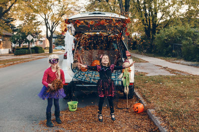 Full length of cute girls standing by car at road