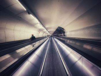 Light trails on escalator in illuminated underground walkway