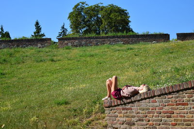 Woman lying on retaining wall against sky