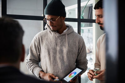 Male entrepreneur holding digital tablet while standing by colleague during meeting in creative office