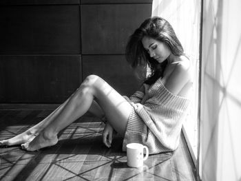 Side view of young woman sitting by coffee cup on floor