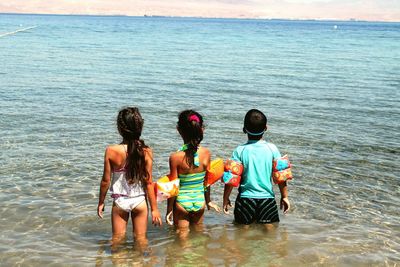 Rear view of boy and girls standing in water on sunny day
