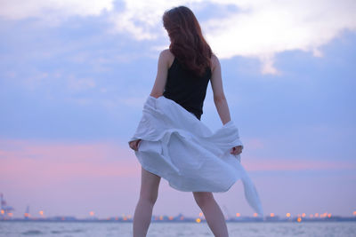 Woman standing at beach against sky during sunset