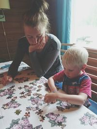 Boy assembling jigsaw puzzle while sitting by mother at table