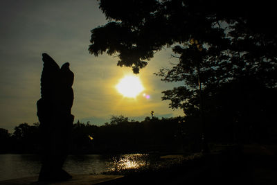 Silhouette trees by lake against sky during sunset