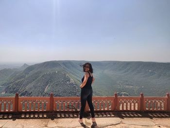 Full length of woman standing on railing against mountains