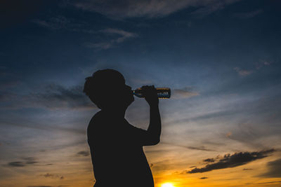 Silhouette man drinking water against sky during sunset