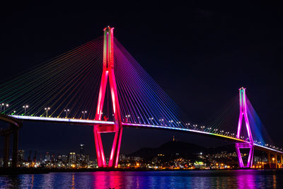 Illuminated bridge over river against sky at night