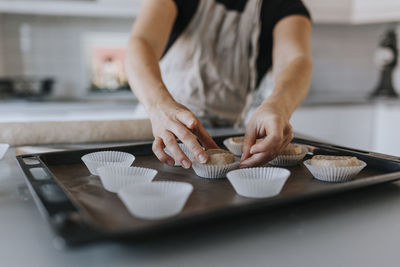 View of woman's hands putting raw cinnamon bun into cupcake case