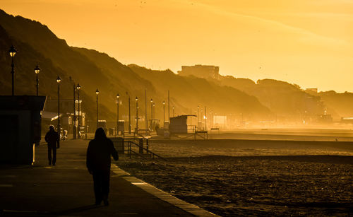 Silhouette people by sea against sky during sunset