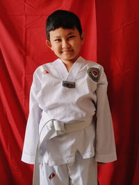 Portrait of boy standing against red curtain