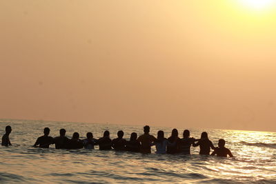 Silhouette people on sea against orange sky