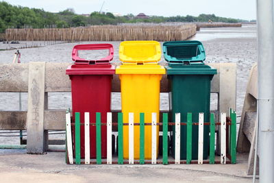 Multi colored garbage bins by fence against field