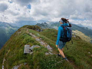 Rear view of woman hiking on rocky mountain peak against sky