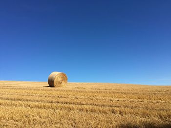 Hay bales on field against clear blue sky