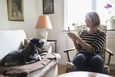 Senior woman photographing dog through smart phone at home