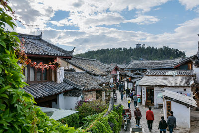 People walking on street amidst old houses in town against sky