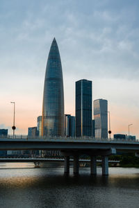 Bridge over river against buildings in city at sunset