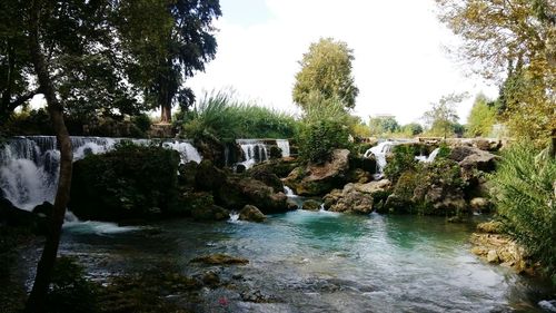 Scenic view of waterfall in forest against sky