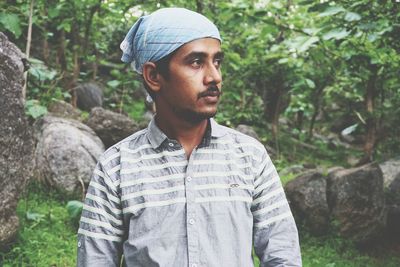 Young man looking away while standing in forest