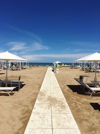 Footpath and sunshades on beach against blue sky