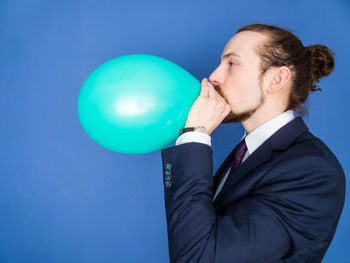 Side view of businessman blowing green balloon against blue background