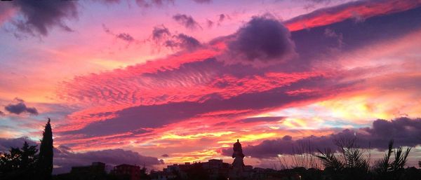 Silhouette of city against cloudy sky during sunset