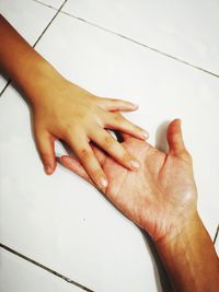 Cropped hands of parent and child on tiled floor at home