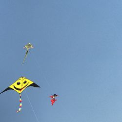 Low angle view of kites against clear blue sky