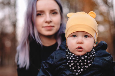 Young mother holding baby boy while sitting in park during autumn