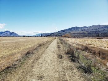 Dirt road leading towards mountains against sky