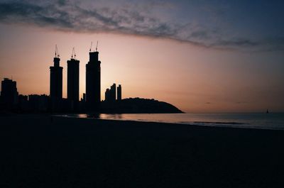 Silhouette of buildings by sea during sunset